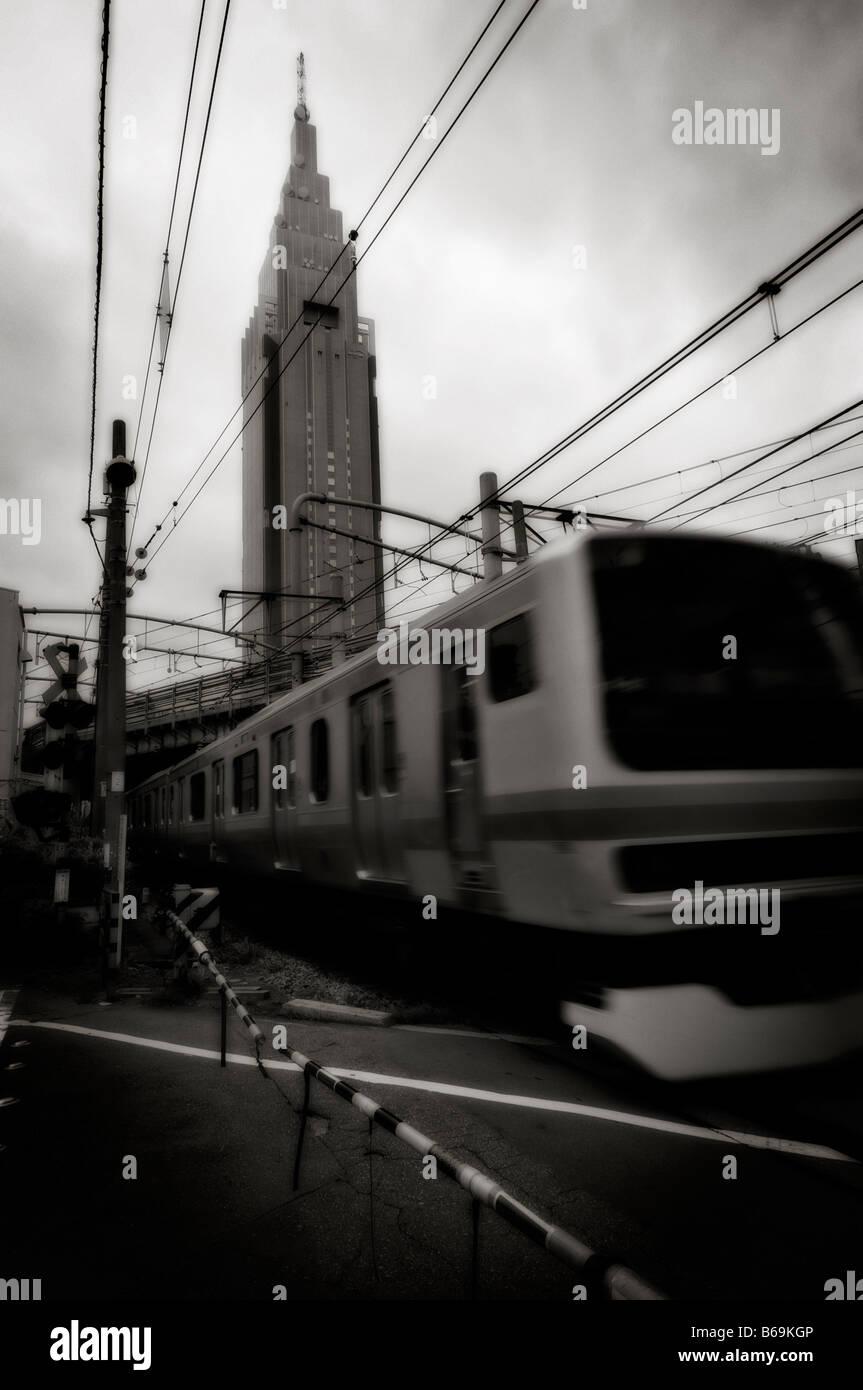 NTT DoCoMo Yoyogi Building (arrière-plan) et d'un train en mouvement sur une route à travers railroad crossing. Shinjuku. Tokyo. Le Japon. Banque D'Images