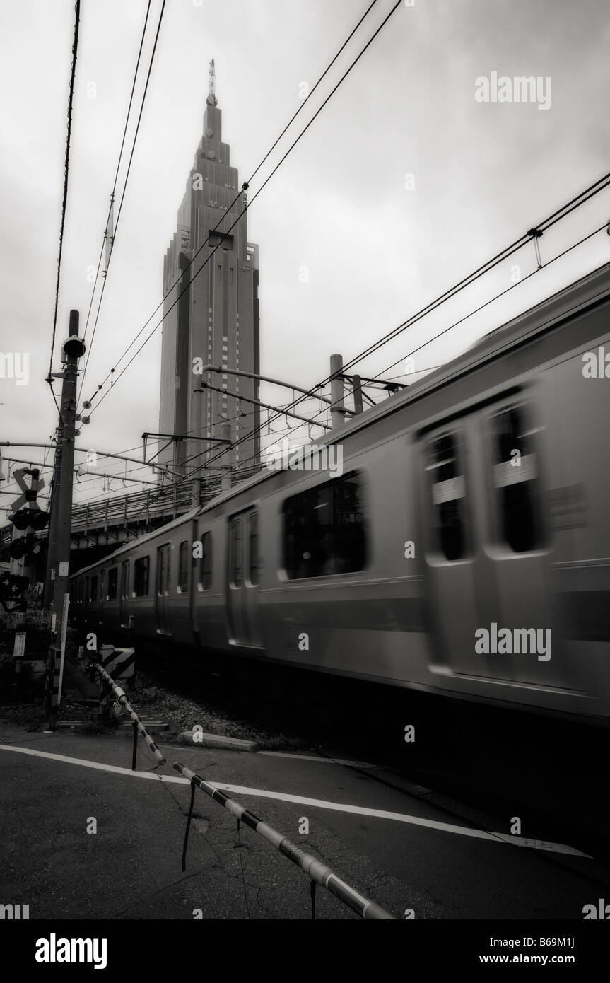 NTT DoCoMo Yoyogi Building (arrière-plan) et d'un train en mouvement sur une route à travers railroad crossing. Shinjuku. Tokyo. Le Japon. Banque D'Images
