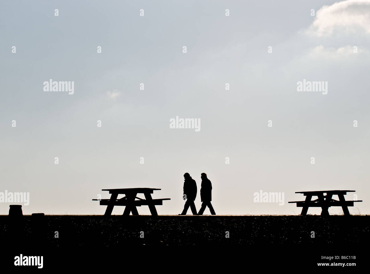 Silhouette de deux personnes marchant entre les tables de pique-nique à Eastbourne dans l'East Sussex. Banque D'Images