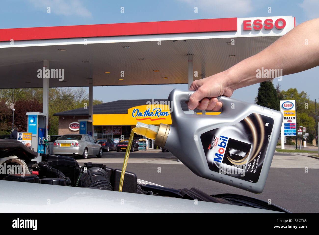 L'huile moteur Mobil 1 est versé dans un moteur de voiture sur un parvis d'essence Esso Banque D'Images