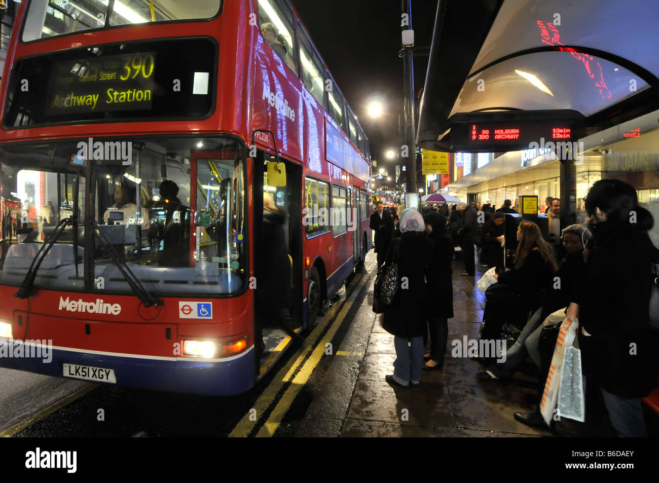 Arrêt de bus d'Oxford Street et passagers du West End Christmas qui attendent à bord du bus 390 et d'autres qui attendent avec horaire électronique Londres Angleterre Royaume-Uni Banque D'Images