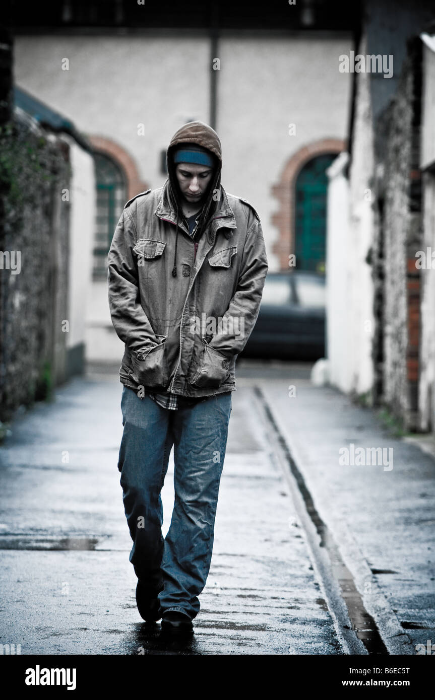 Jeune homme portant une veste seule et isolée dans une ruelle dans une ville en marche vers l'appareil photo Banque D'Images