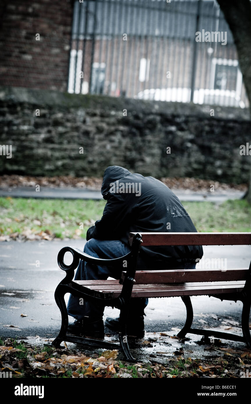 Jeune homme portant une veste à capuchon enfoncé lonely seule et isolée assis sur un banc de parc UK Banque D'Images