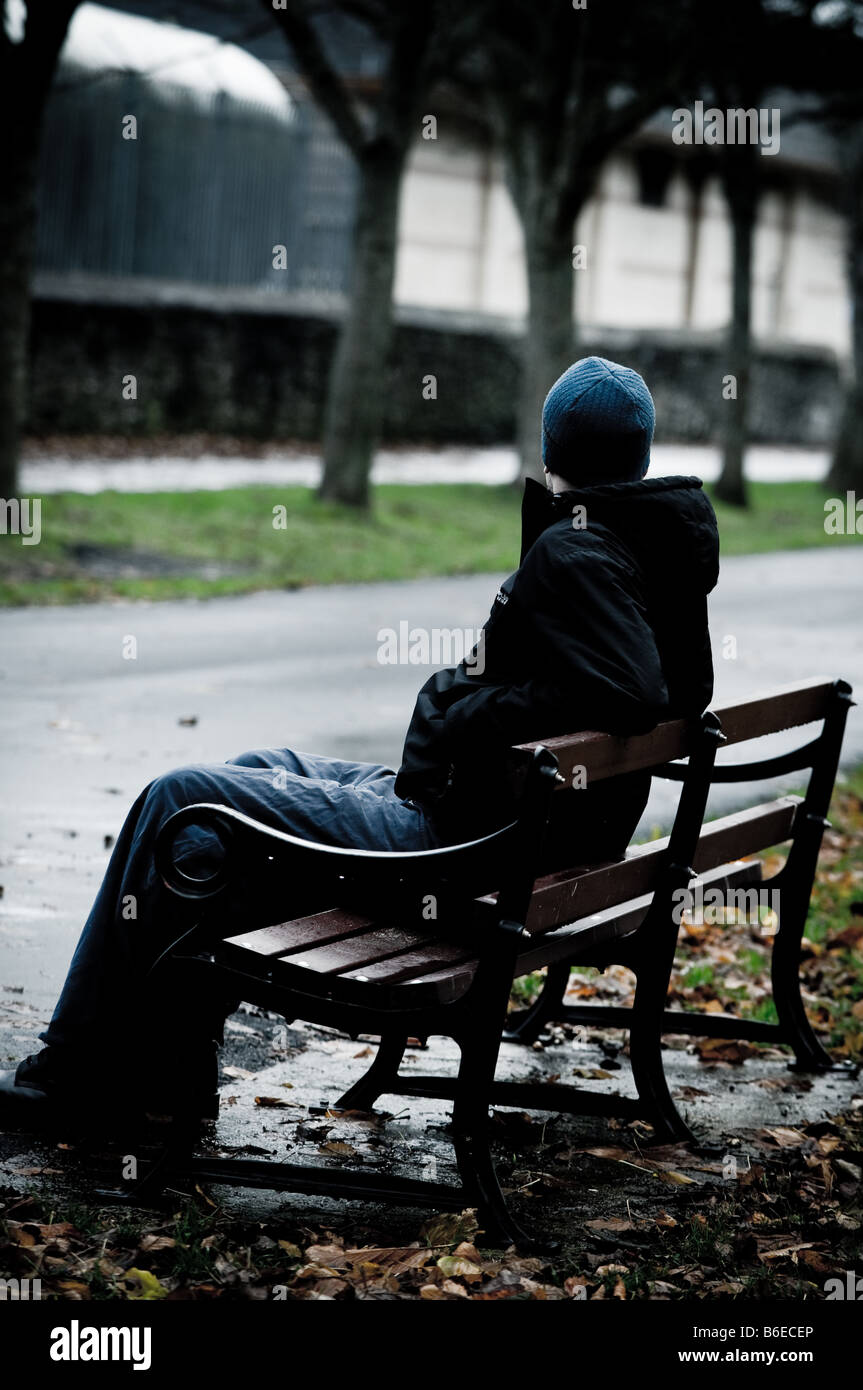 Jeune homme portant une veste seule et isolée assis sur un banc de parc Banque D'Images