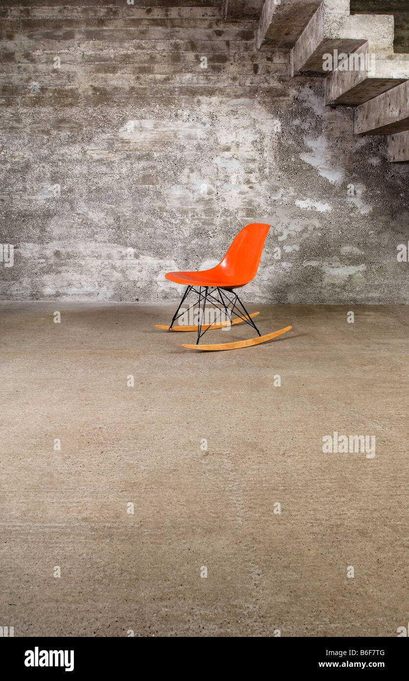 Designer Orange chaise berçante dans une salle vide en face d'un mur de béton Banque D'Images