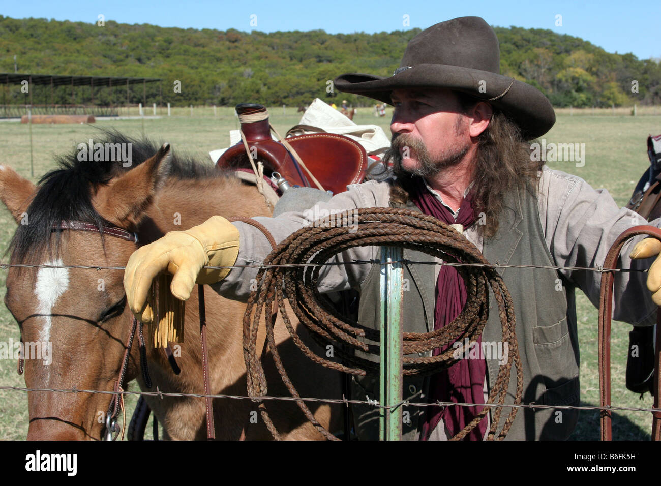 Un cowboy robuste avec son cheval prendre une pause pour travailler le ranch et mettant sa corde sur le barbwire fencepost Banque D'Images
