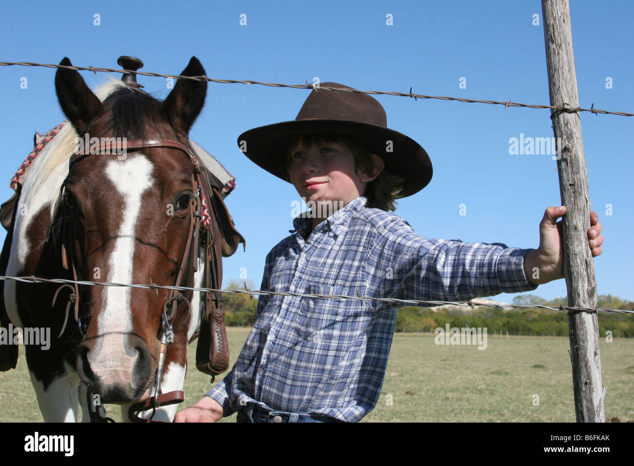 Un jeune cow-boy avec son cheval prendre une pause pour travailler le ranch et s'appuyant sur la clôture de barbelés Banque D'Images