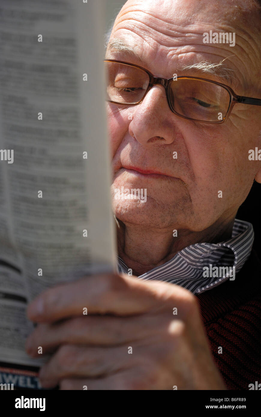 Vieil homme portant des lunettes et lire un journal avec une expression grave, Emmendingen, Bade-Wurtemberg, Allemagne Banque D'Images