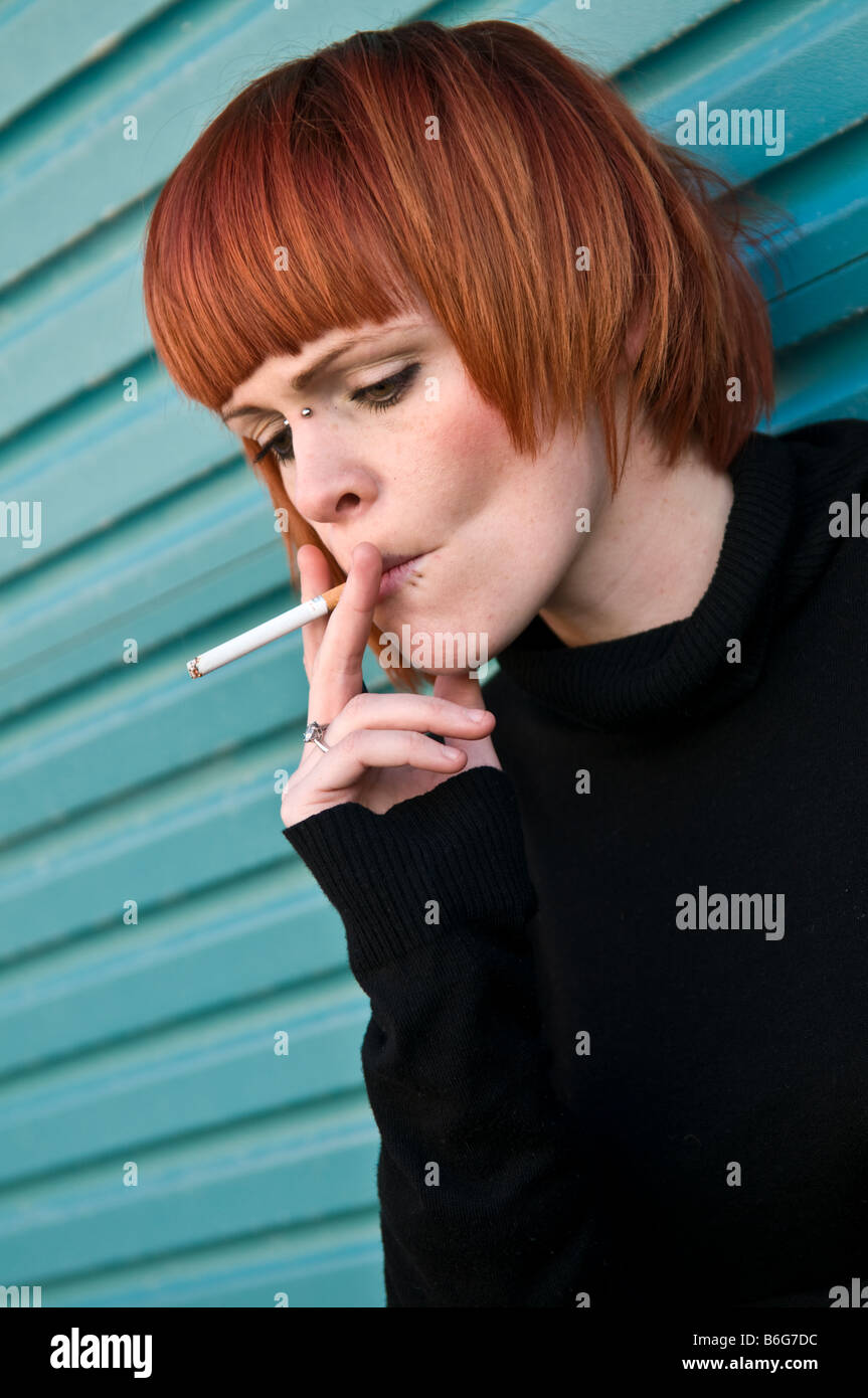 Peau pâle aux cheveux rouge jeune fille femme irlandaise avec une cigarette dans sa bouche, prenant une profonde faites glisser sur sa cigarette Banque D'Images