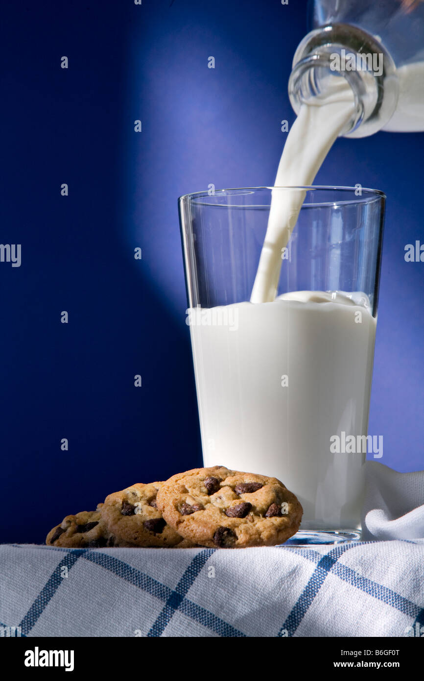 Verre et bouteille de lait avec des cookies sur un fond bleu avec le lait verser Banque D'Images