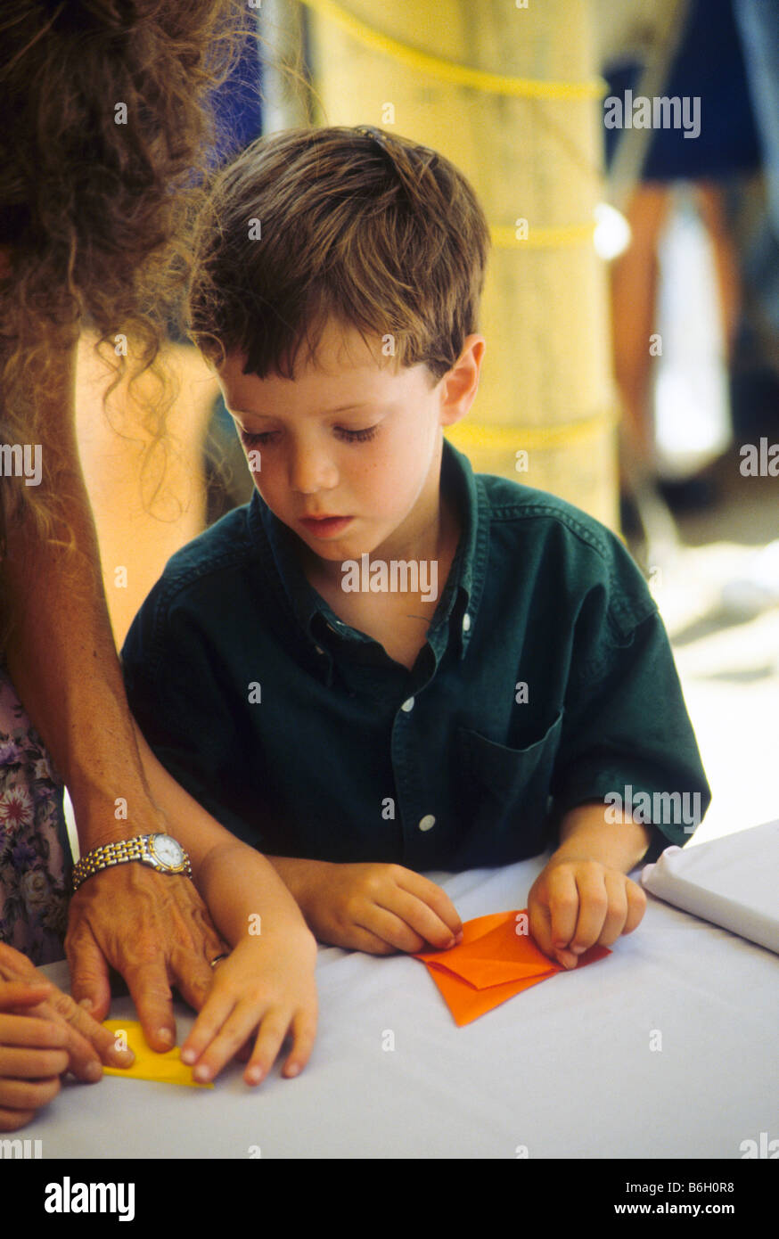 Jeune garçon obtient les conseils de adulte comme il fait le projet d'art du papier plié. Banque D'Images