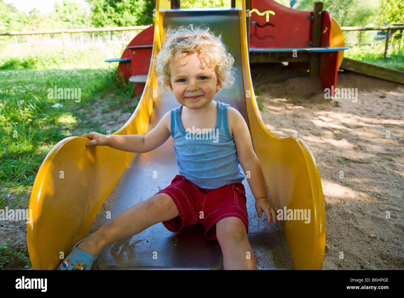 Cute boy sur une diapositive à l'aire de jeux Banque D'Images