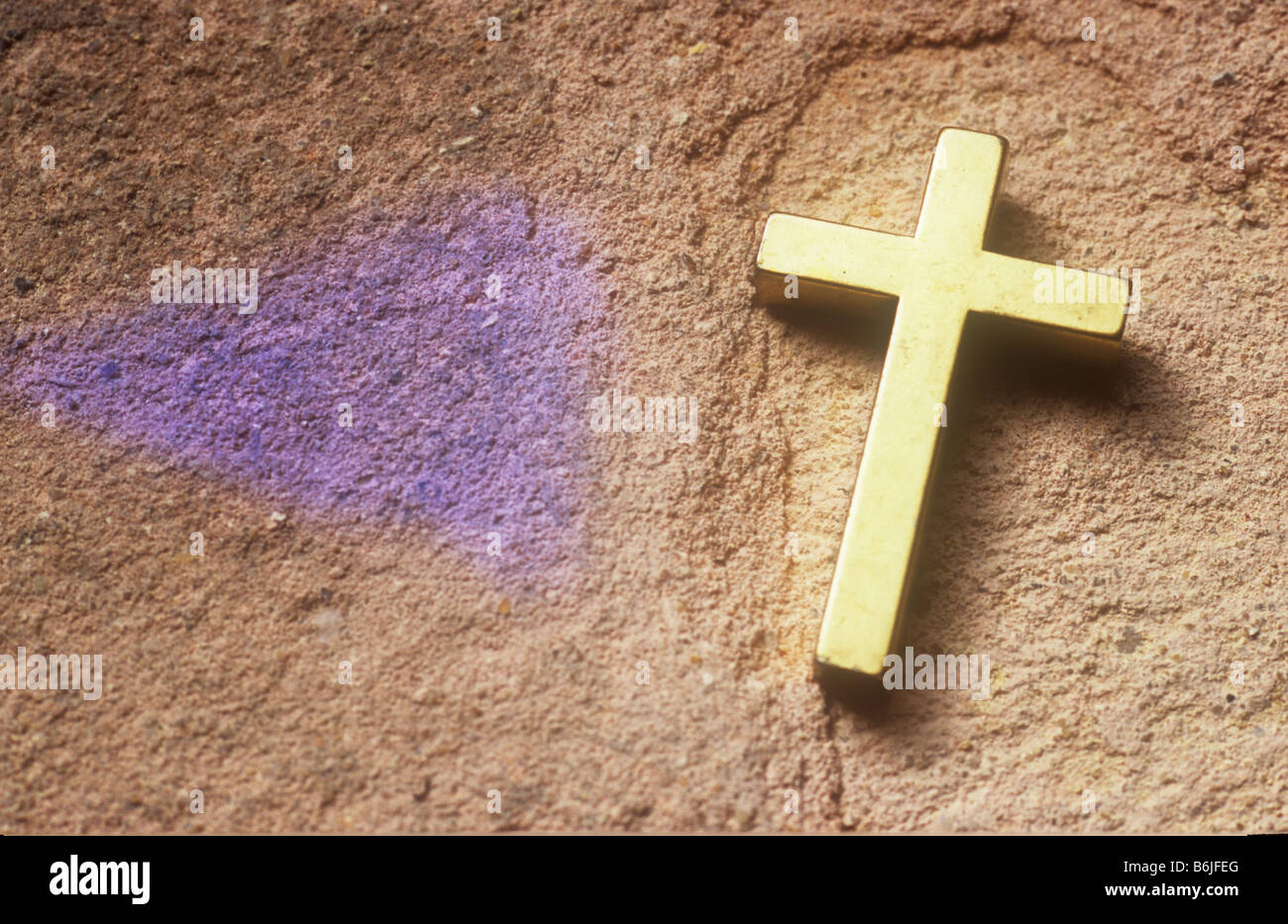 Close up d'un crucifix d'or couché sur la surface rugueuse de la pierre rose mauve avec coin de lumière projetée à proximité Banque D'Images