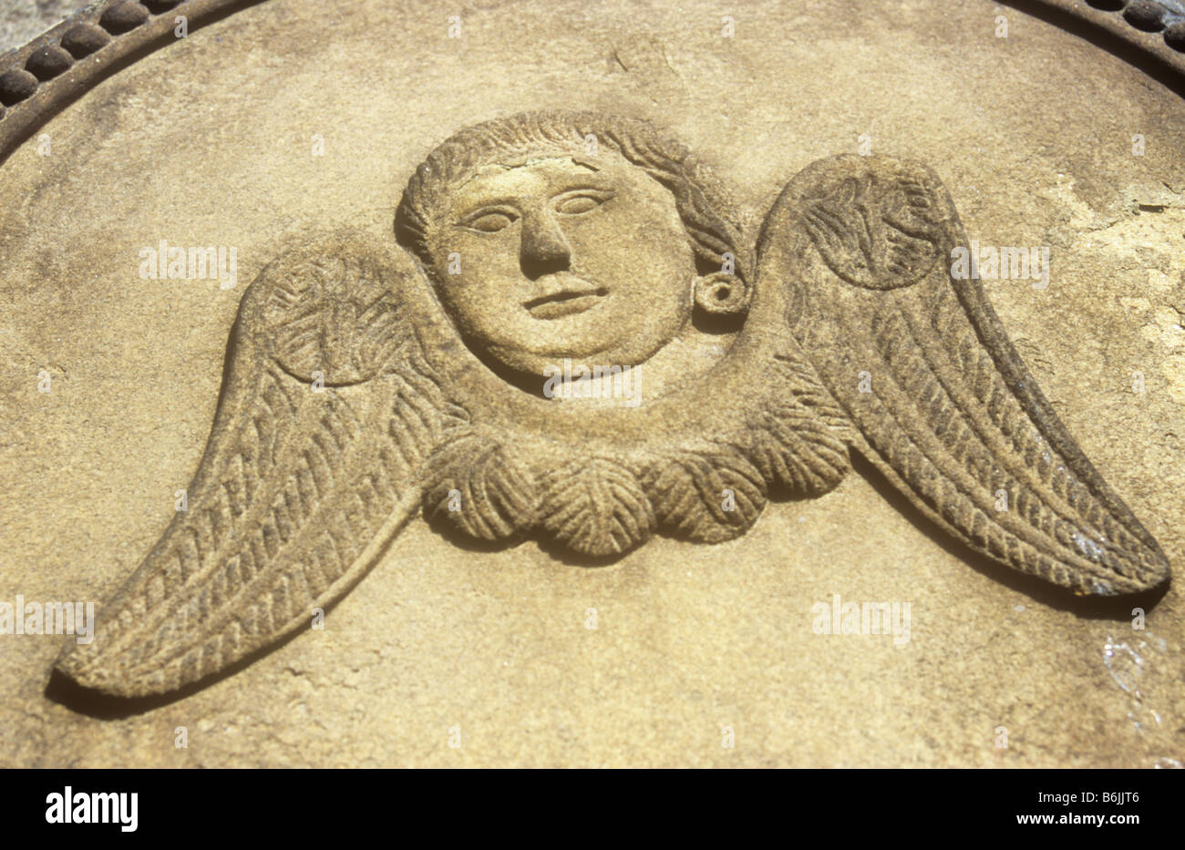 Détail de la pierre tombale en grès sculpté dans la lumière chaude de style naïf avec tête désincarnée et ailes d'un ange Banque D'Images