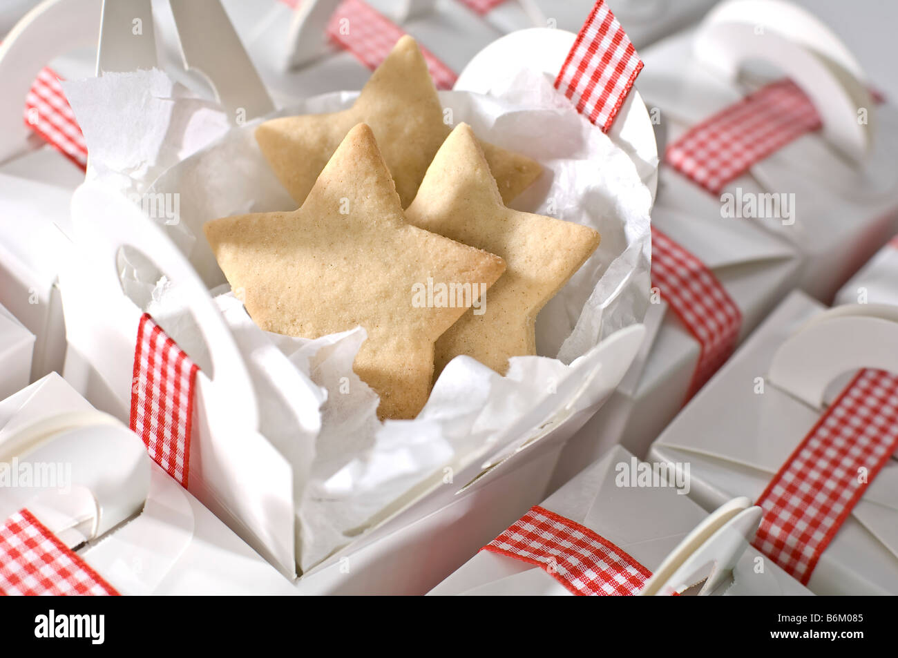 Découper des biscuits en forme d'étoile d'être emballés dans de simples boîtes blanc ordinaire pour les cadeaux à Noël. Attachés avec du ruban vichy rouge Banque D'Images