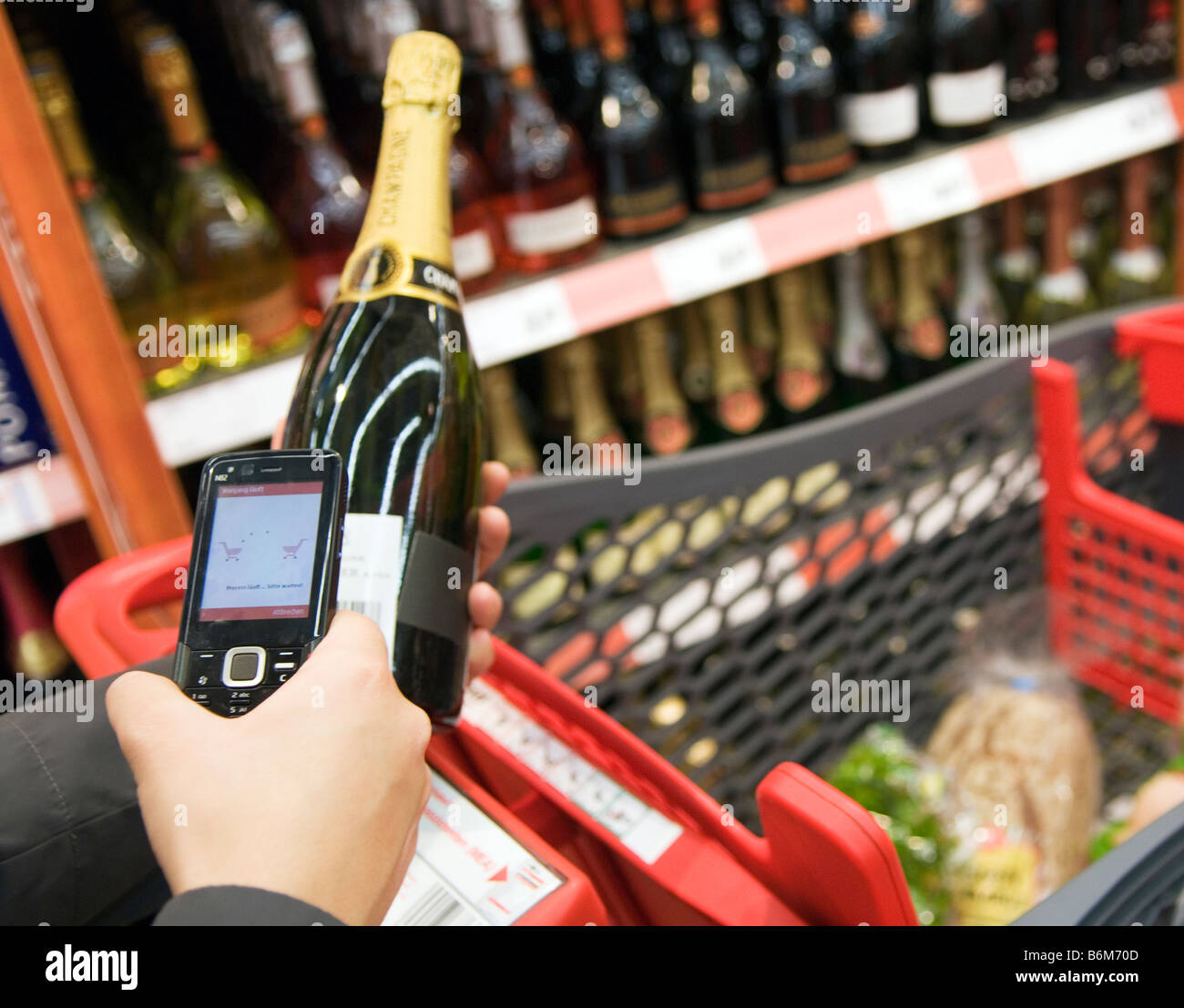 Jeune femme analyse le prix d'une bouteille de champagne dans son téléphone cellulaire dans un supermarché Banque D'Images