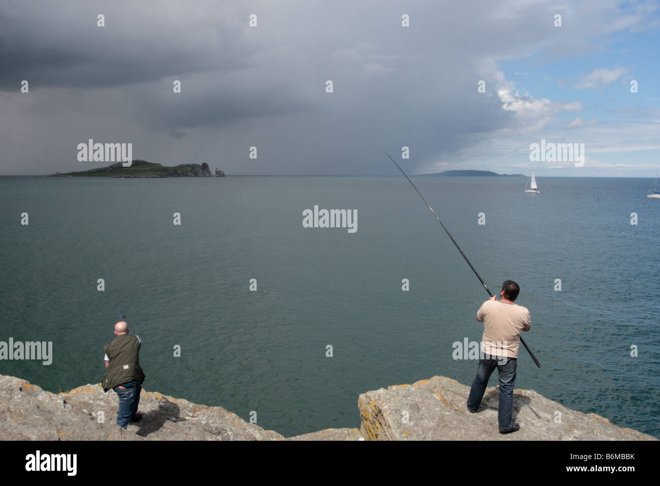 Deux pêcheurs jeter leurs lignes comme des nuages de pluie sur la baie de Dublin vu de Howth Banque D'Images