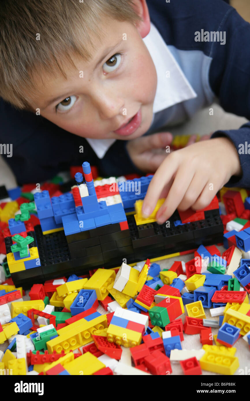 Jeune garçon de huit ans couché jouant avec des briques de construction de jouets. Banque D'Images