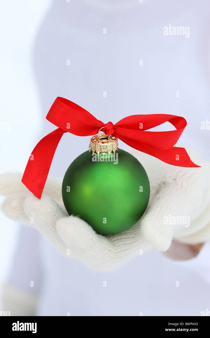 Les mains avec des gants hiver holding Christmas Ornament with bow Banque D'Images