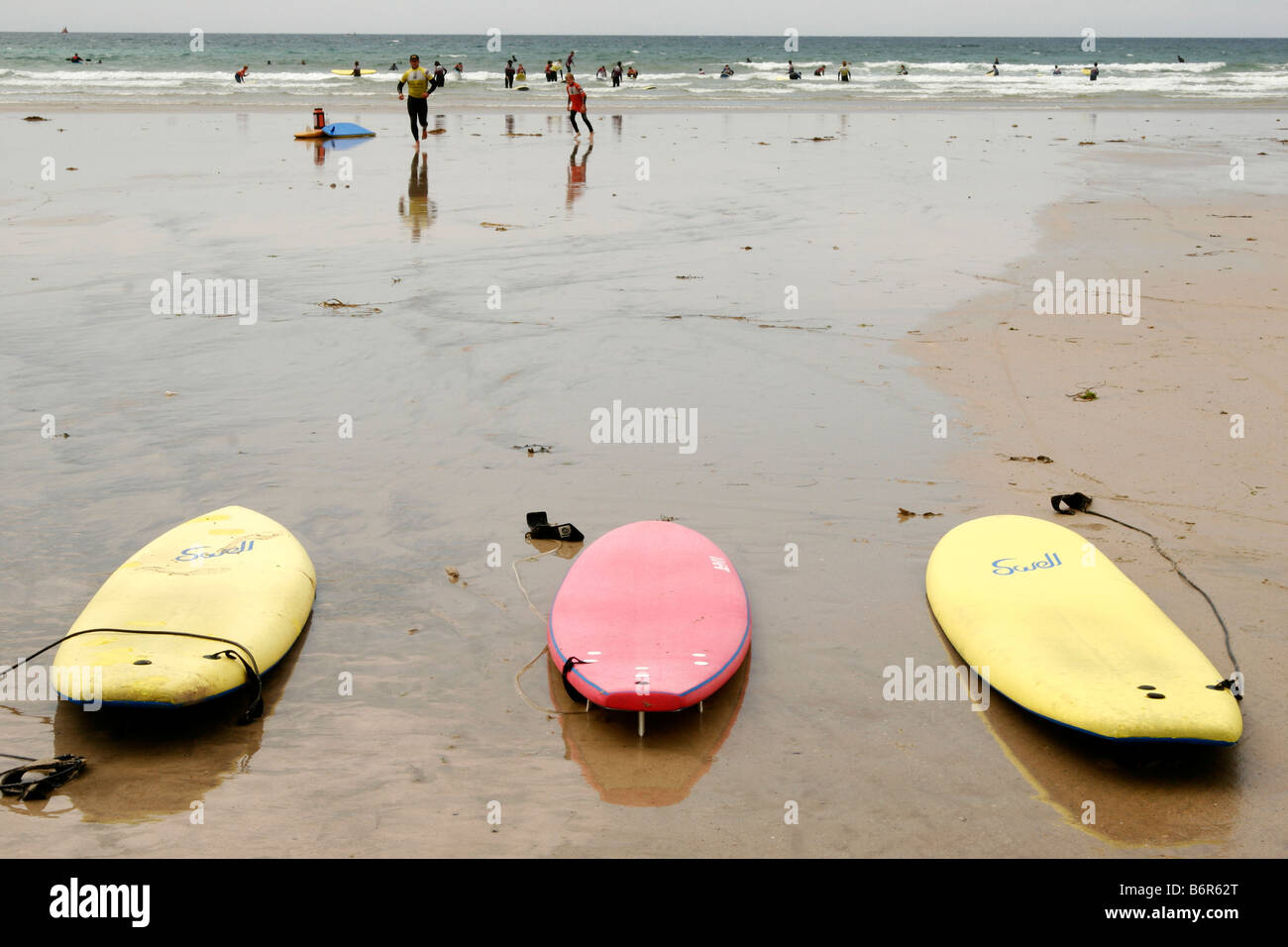 Trois planches posées sur une plage de sable fin, prêt à être utilisé, avec des gens le surf et natation, à Polzeath, Cornwall, Angleterre Banque D'Images