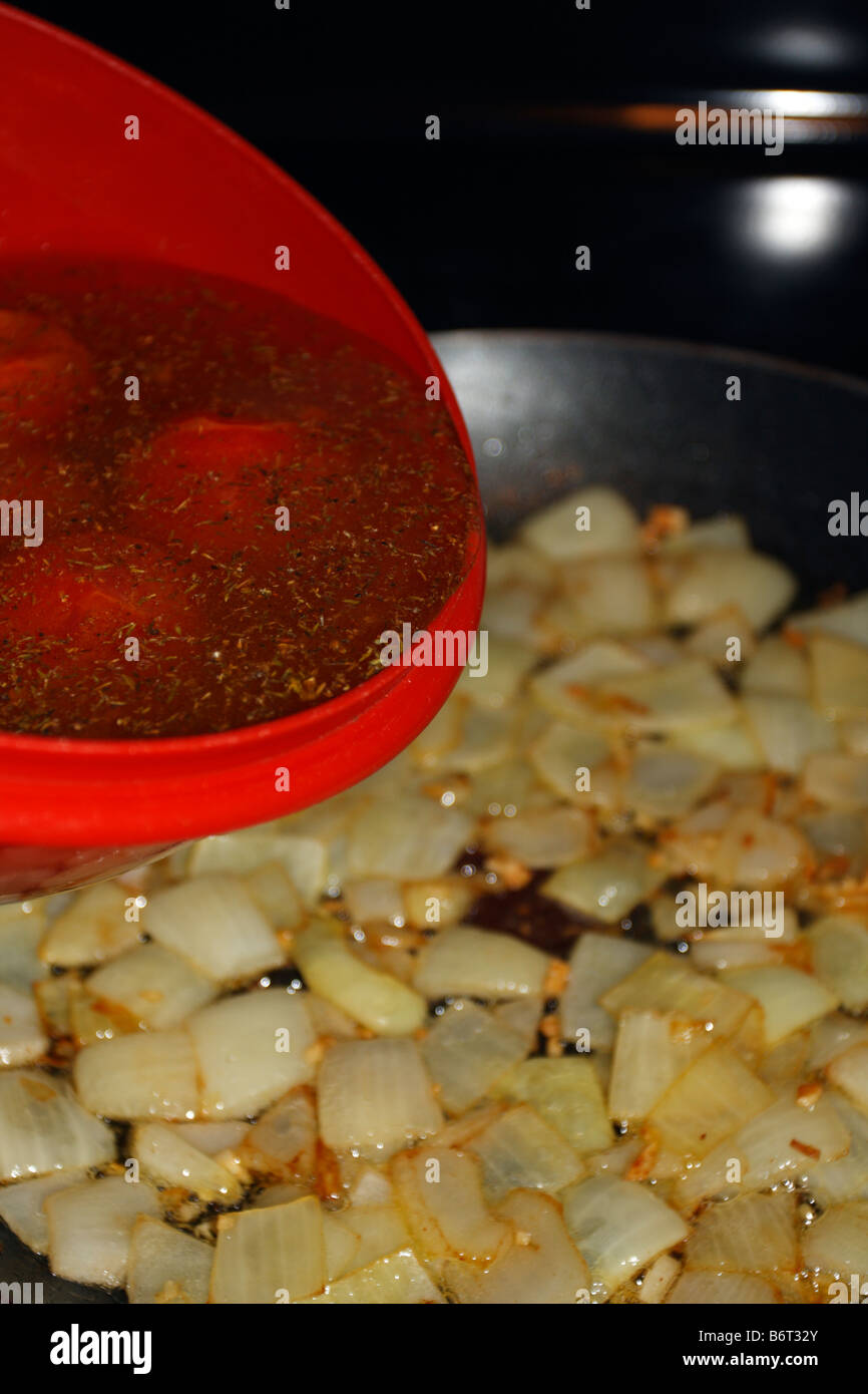 L'eau, les épices, et les tomates dans le bol au-dessus doré oignons en cubes. Banque D'Images