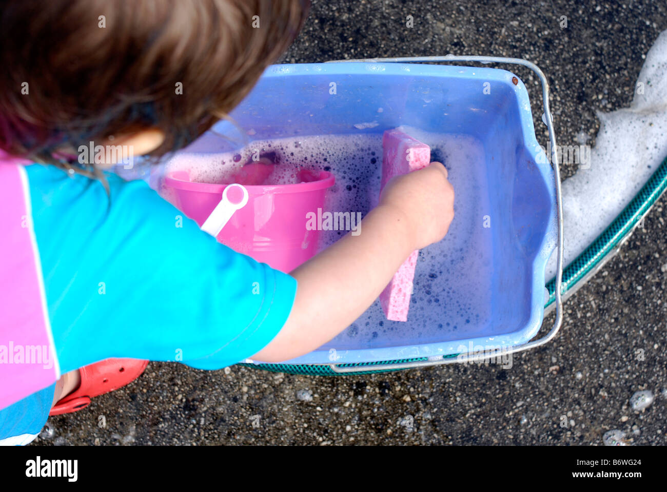 Fillette de deux ans s'amusant à jouer avec de l'eau savonneuse tout en aidant à se laver la voiture familiale Banque D'Images
