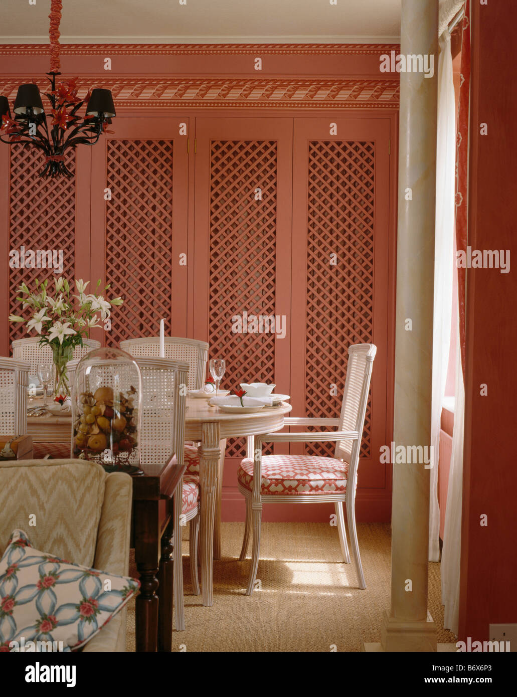 Rose équipé armoire avec portes en ajouré de style gustavien en salle à manger avec chaises blanches et tapis en sisal Banque D'Images