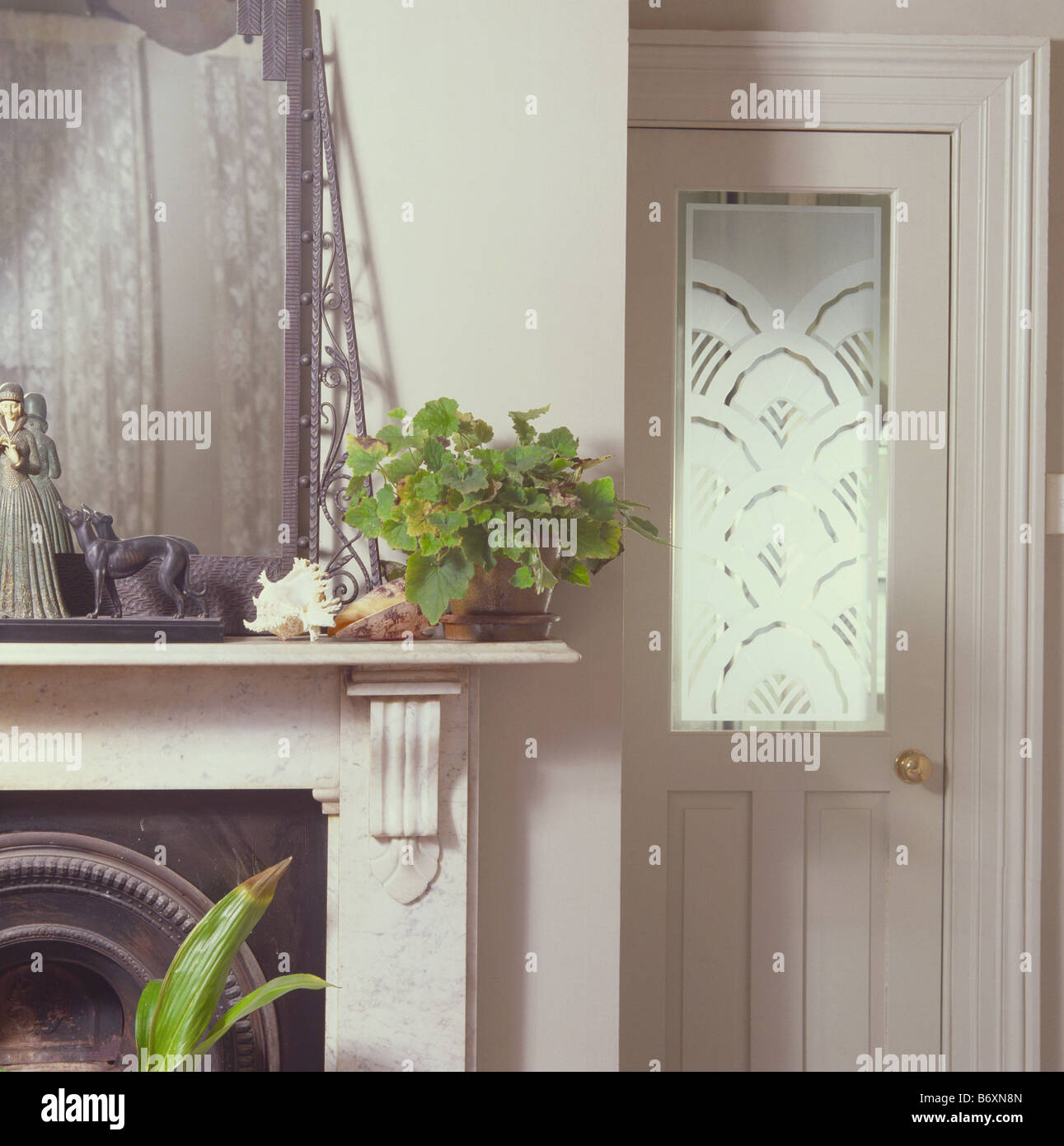 Salon avec close-up de miroir et plante verte sur la cheminée en marbre blanc à côté de porte avec panneau en verre gravé Banque D'Images