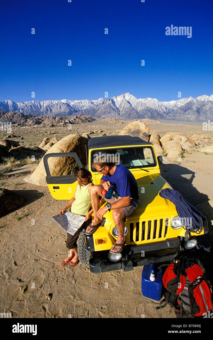 L'homme et la femme traînant sur le capot d'une jeep dans le désert, à côté de la montagne. Banque D'Images