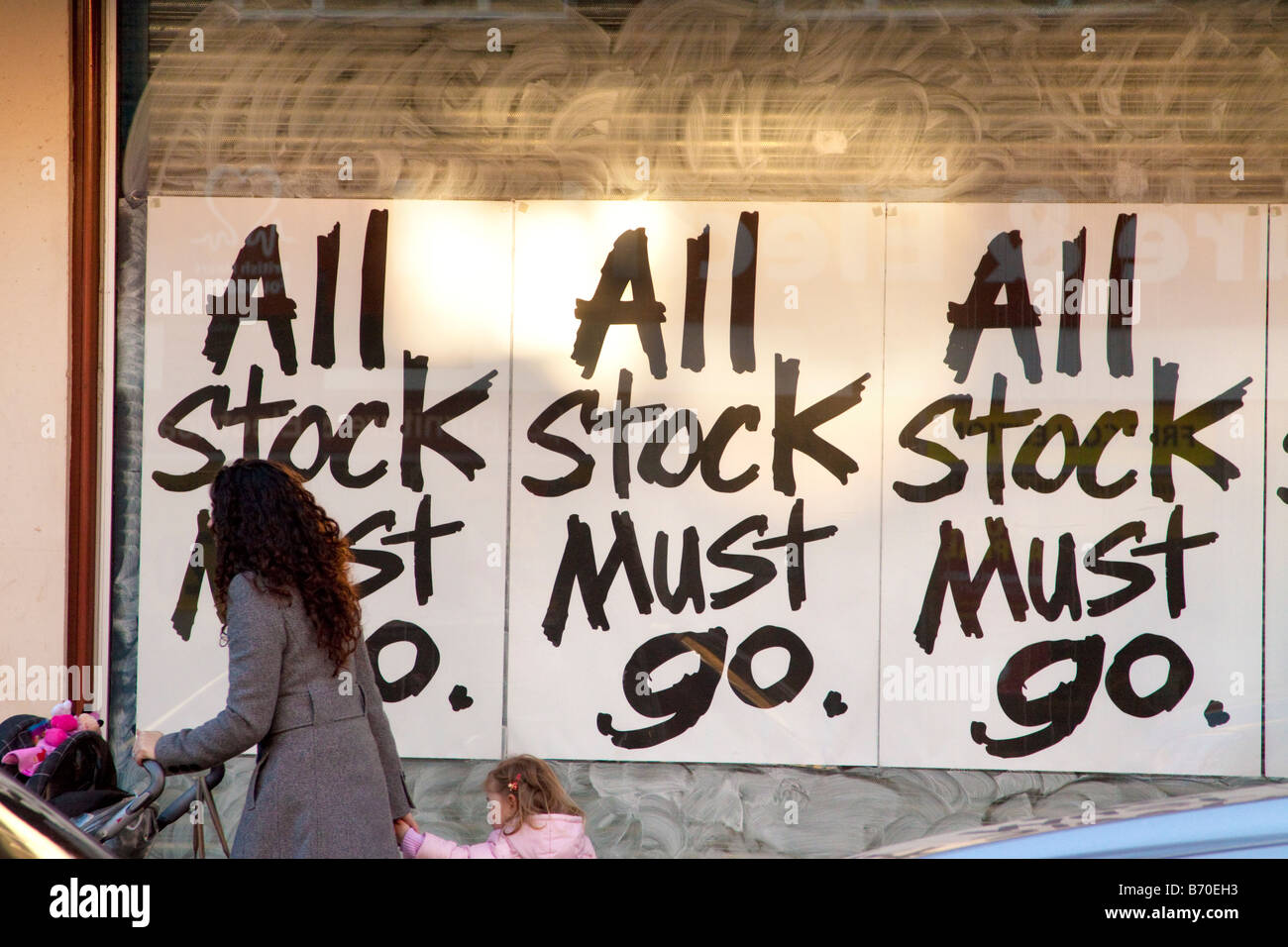 Tous LES STOCKS DOIVENT ALLER EN SIGNES DE VENTE VITRINE AVEC LA MÈRE ET LES ENFANTS PASSANT Banque D'Images