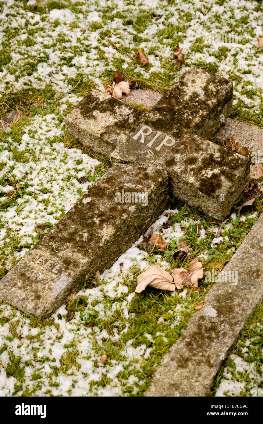 Une pierre tombale en forme de croix portant le sigle 'RIP' cassé, couché sur le sol. Banque D'Images