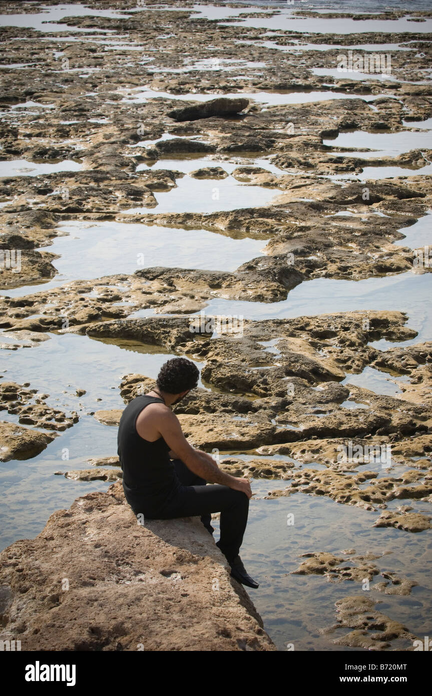 Homme seul assis sur la roche par la mer Banque D'Images