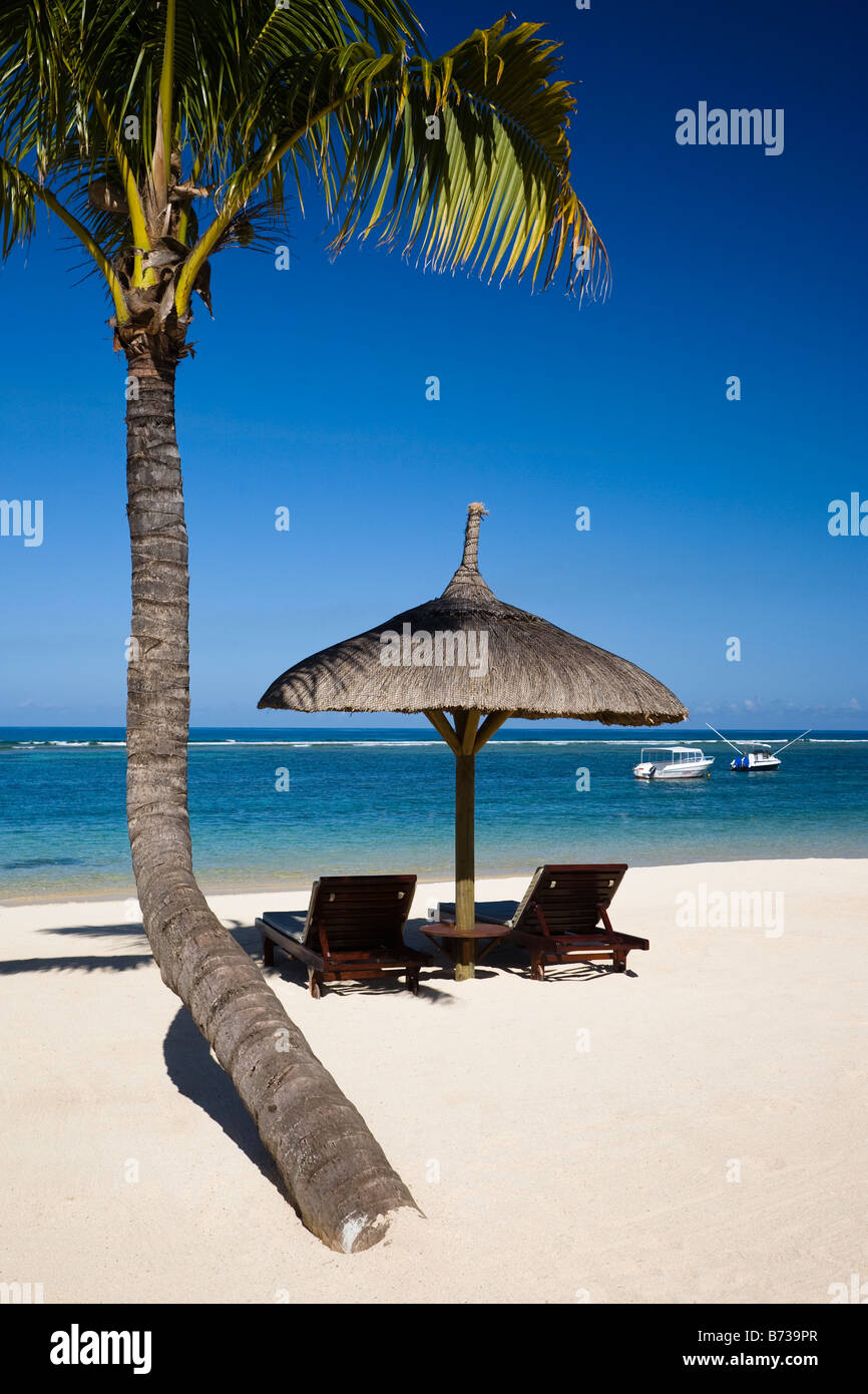Plage de l'Ile Maurice avec vue sur l'Océan Indien avec deux lits et l'ombre sous un palmier et deux bateaux à la distance Banque D'Images