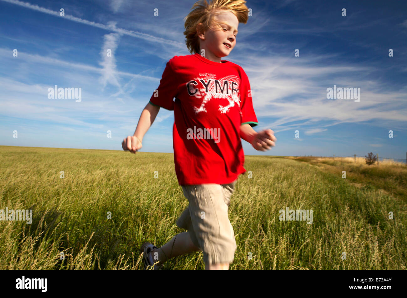 Jeune garçon courir à travers un champ d'herbe dans un T shirt Cymru chemin côtier du Glamorgan près de Nash Point Sud du Pays de Galles Banque D'Images