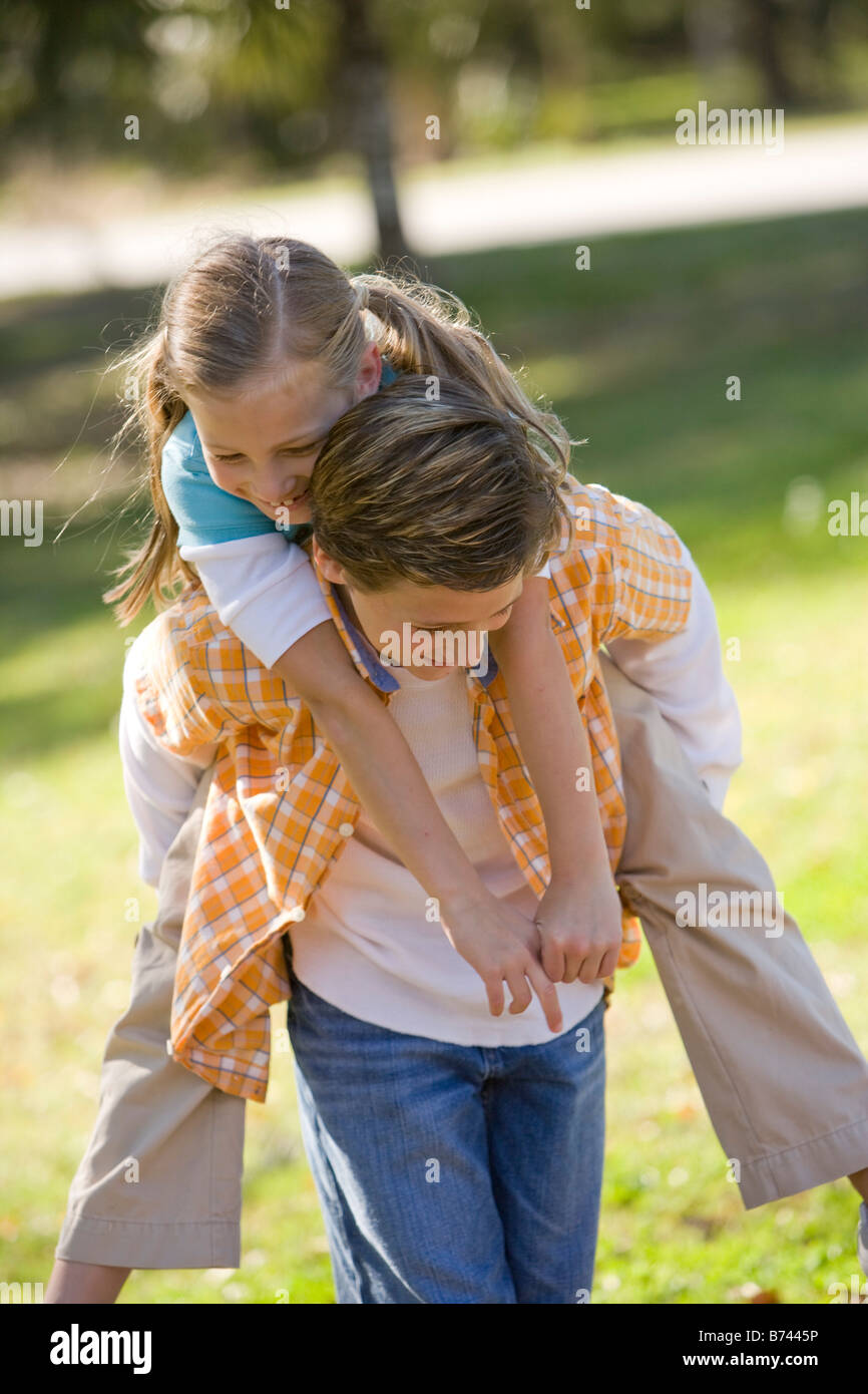 Boy giving piggyback ride à girl in park Banque D'Images