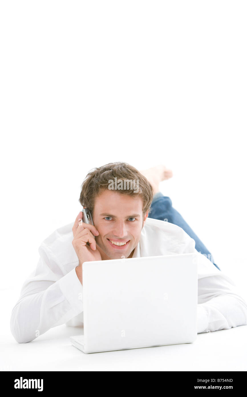 L'un mid adult man lying on floor on the phone with laptop Banque D'Images