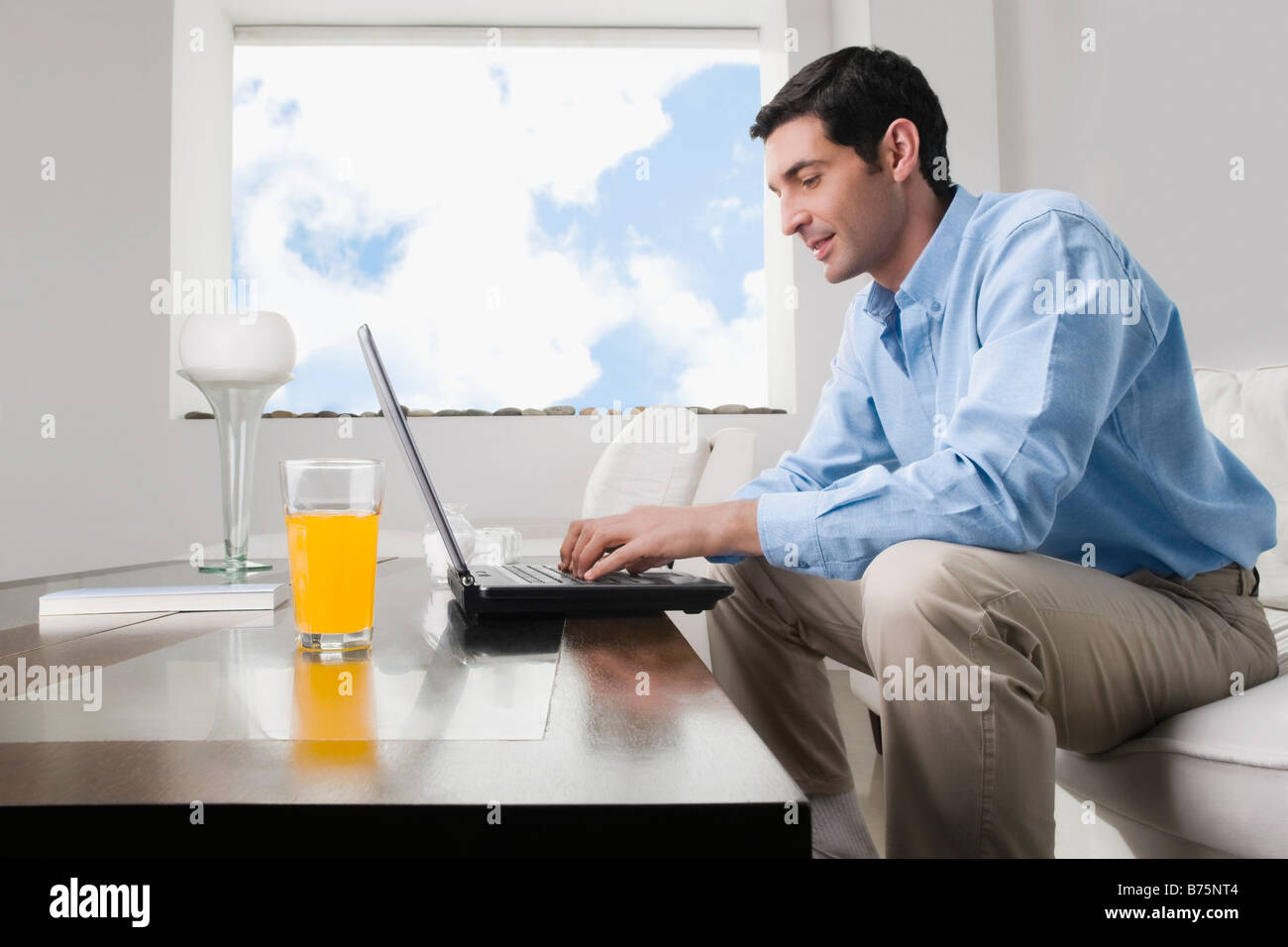 Mid adult man travaille sur un ordinateur portable avec un verre de jus sur la table Banque D'Images