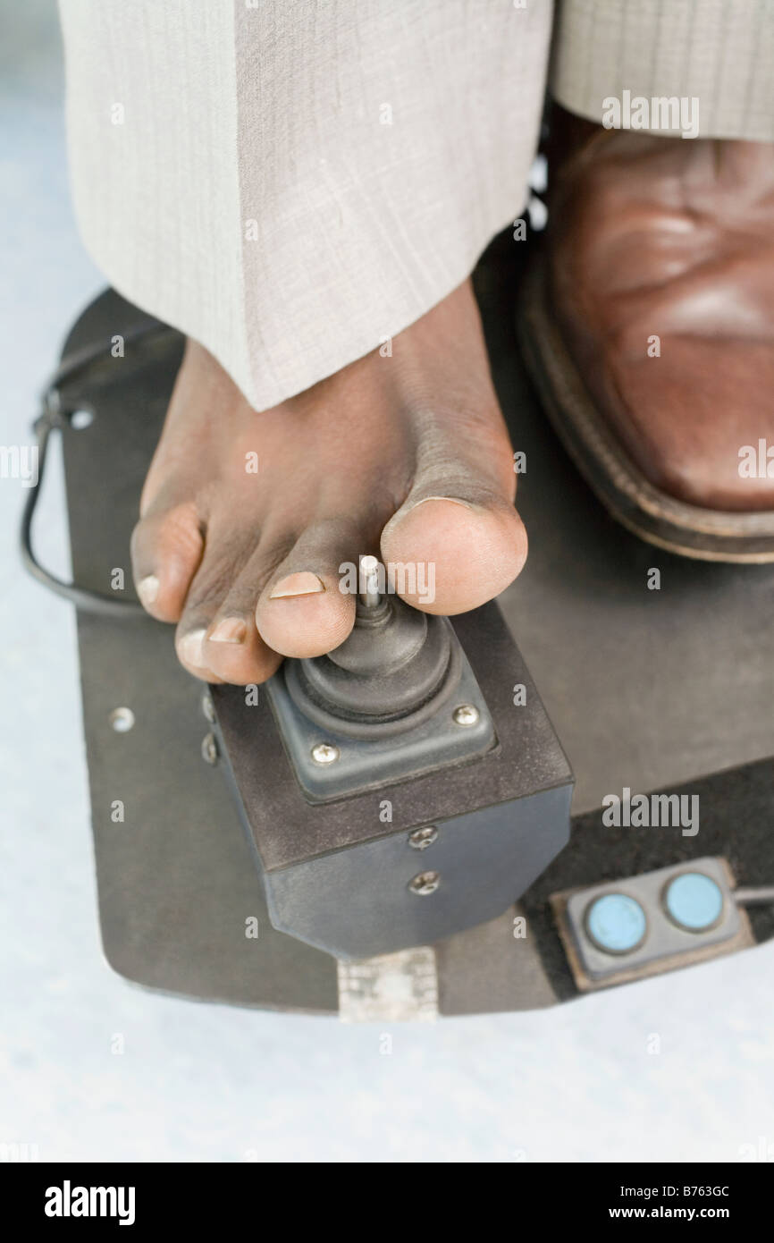 L'homme souffrant de paralysie cérébrale déménagement fauteuil roulant motorisé avec son pied Banque D'Images