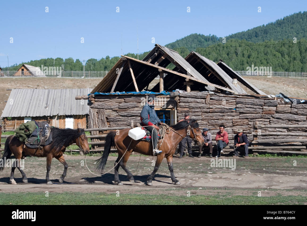 Tuwa herder équitation passé un groupe d'hommes en dehors d'un log cabin en village de Hemu Kanas Parc National dans le Xinjiang en Chine Banque D'Images