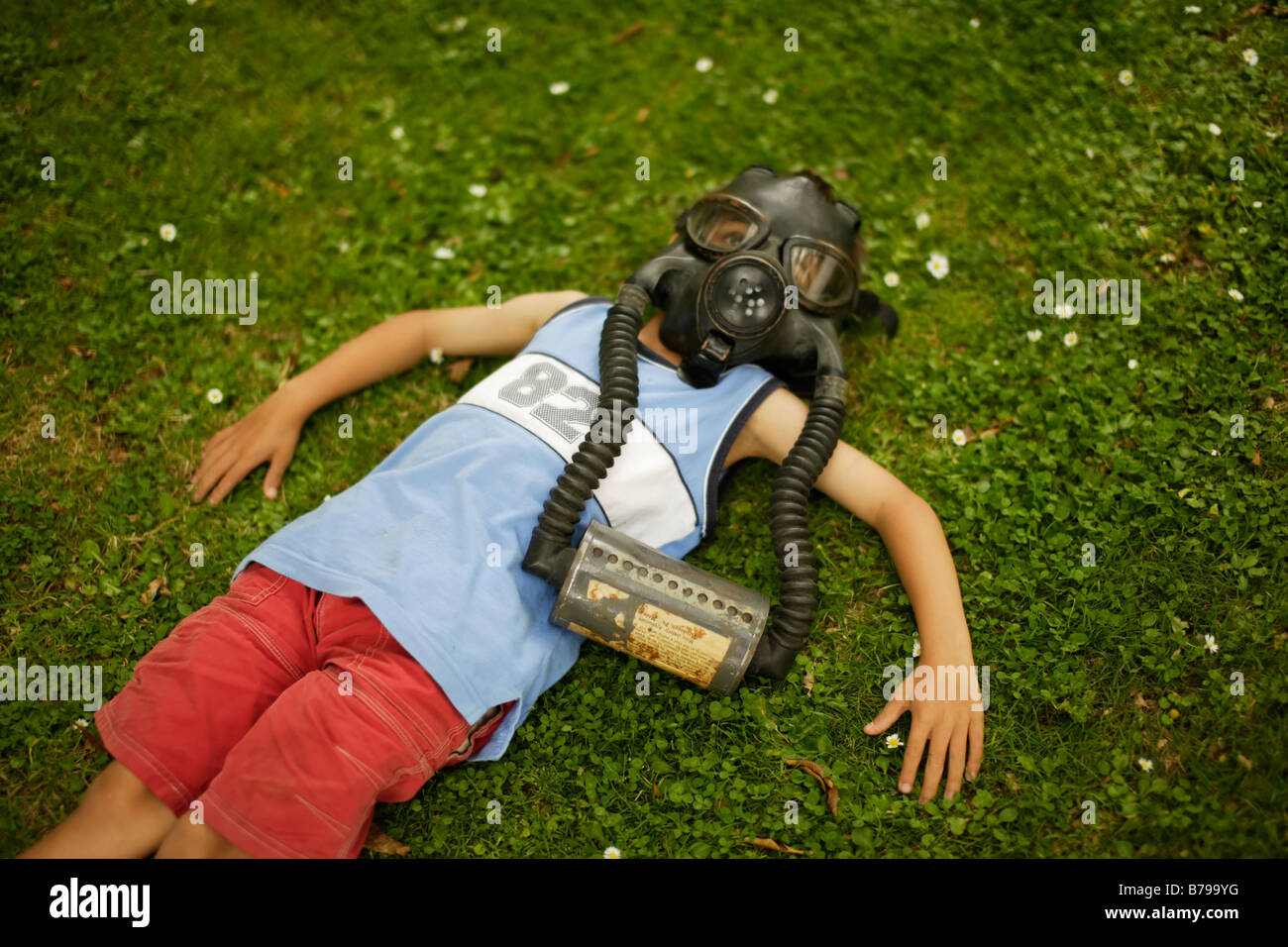 Un garçon de six ans se trouve sur l'herbe verte portant le masque à gaz Banque D'Images