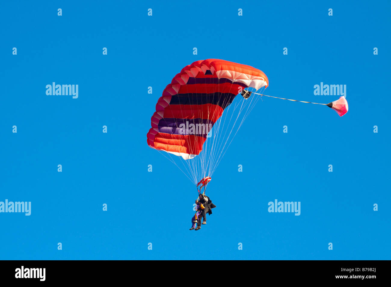 Parachutisme EN TANDEM EN ANGLETERRE Un parachute à rayures rouge transportant deux personnes GLISSE SUR LE CIEL BLEU Banque D'Images