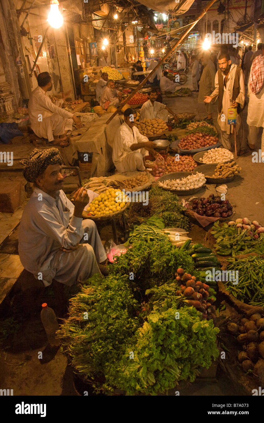 Un vendeur de rue de fumer une cigarette et la vente de légumes dans la nuit dans le vieux bazar à Rawalpindi au Pakistan Banque D'Images