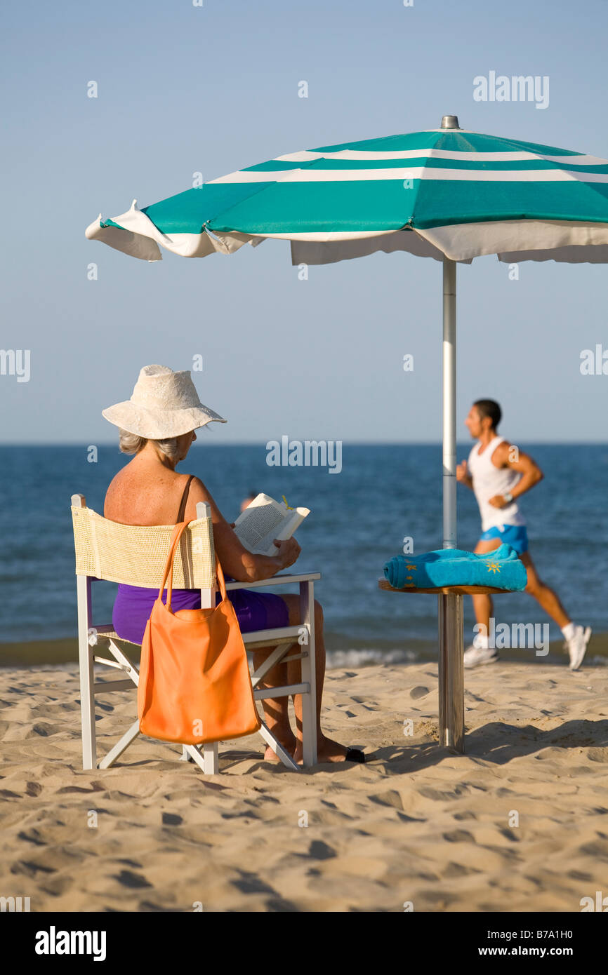 Personne âgée dame livre de lecture à la plage et jogger dans l'arrière-plan Banque D'Images