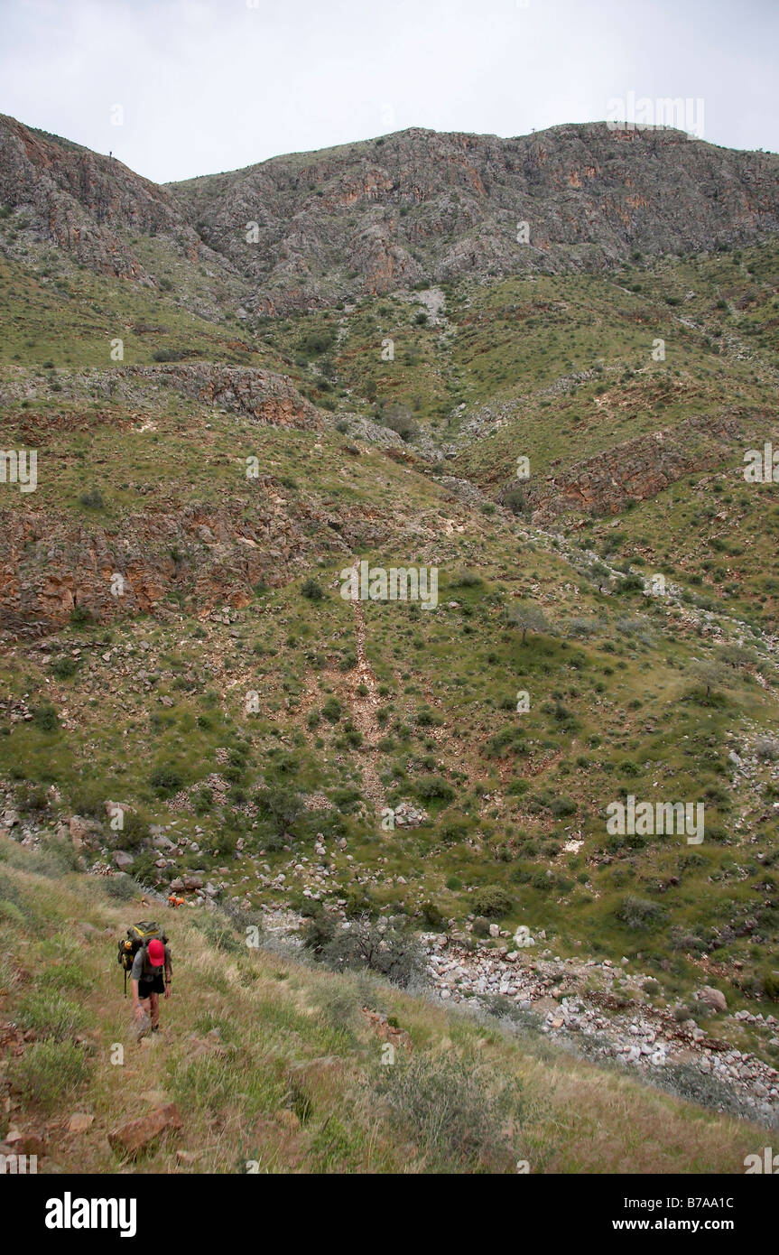 Un adolescent dans un bouchon rouge, l'ascension d'une voie sur une pente rocheuse, sur le sentier de randonnée Naukluft Banque D'Images
