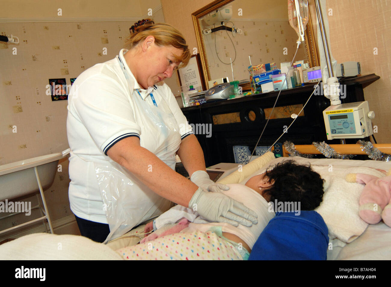 Une infirmière communautaire en ce qui concerne un enfant handicapé profondément dans son lit à la maison modèle Bradford publié Banque D'Images