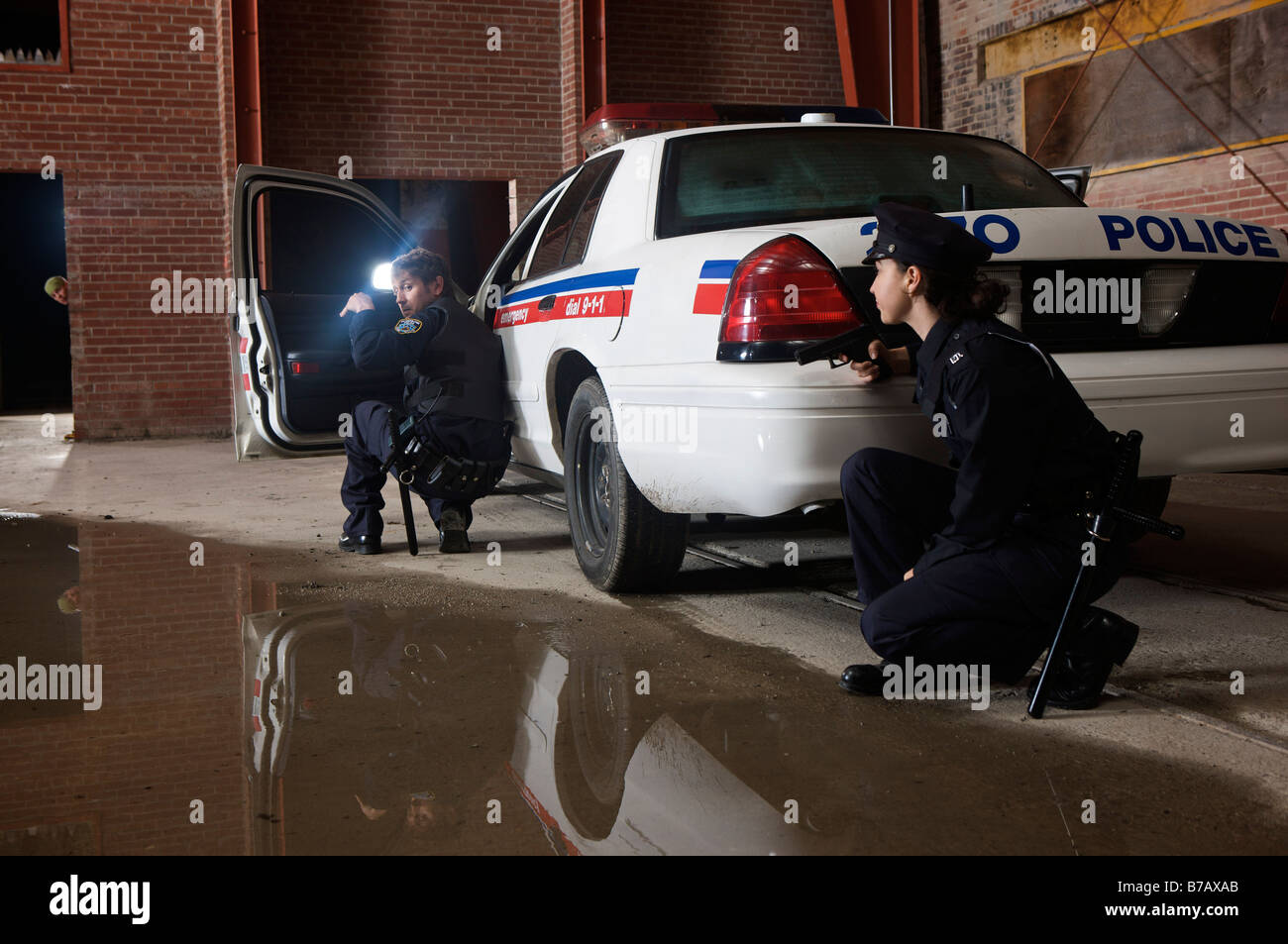 Les agents de police accroupi derrière une voiture de police avec l'arme au poing Banque D'Images