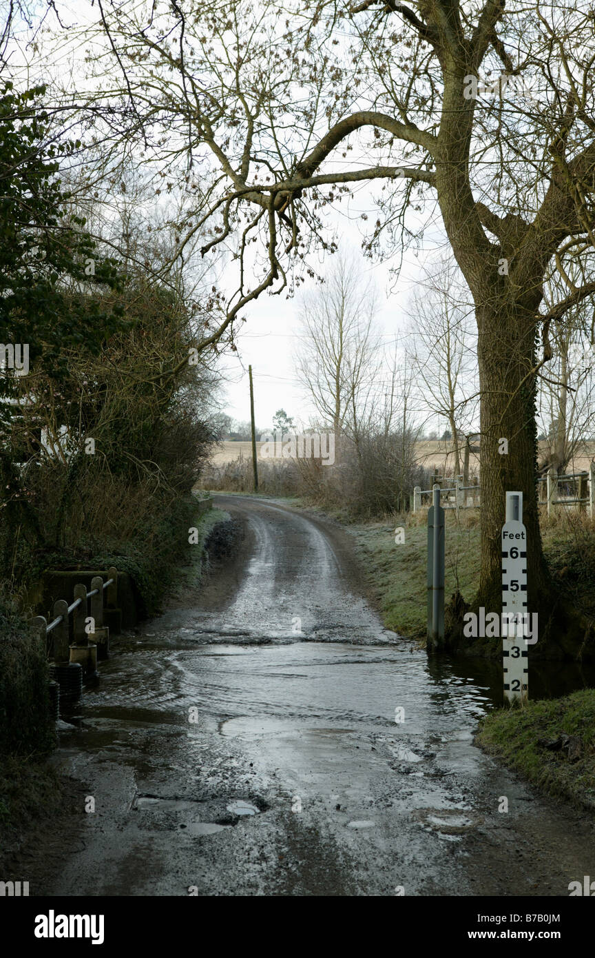 Un pays rural rivière traversant une route avec une hauteur graphique à côté d'un arbre montrant les niveaux d'inondation de la rivière possible Banque D'Images