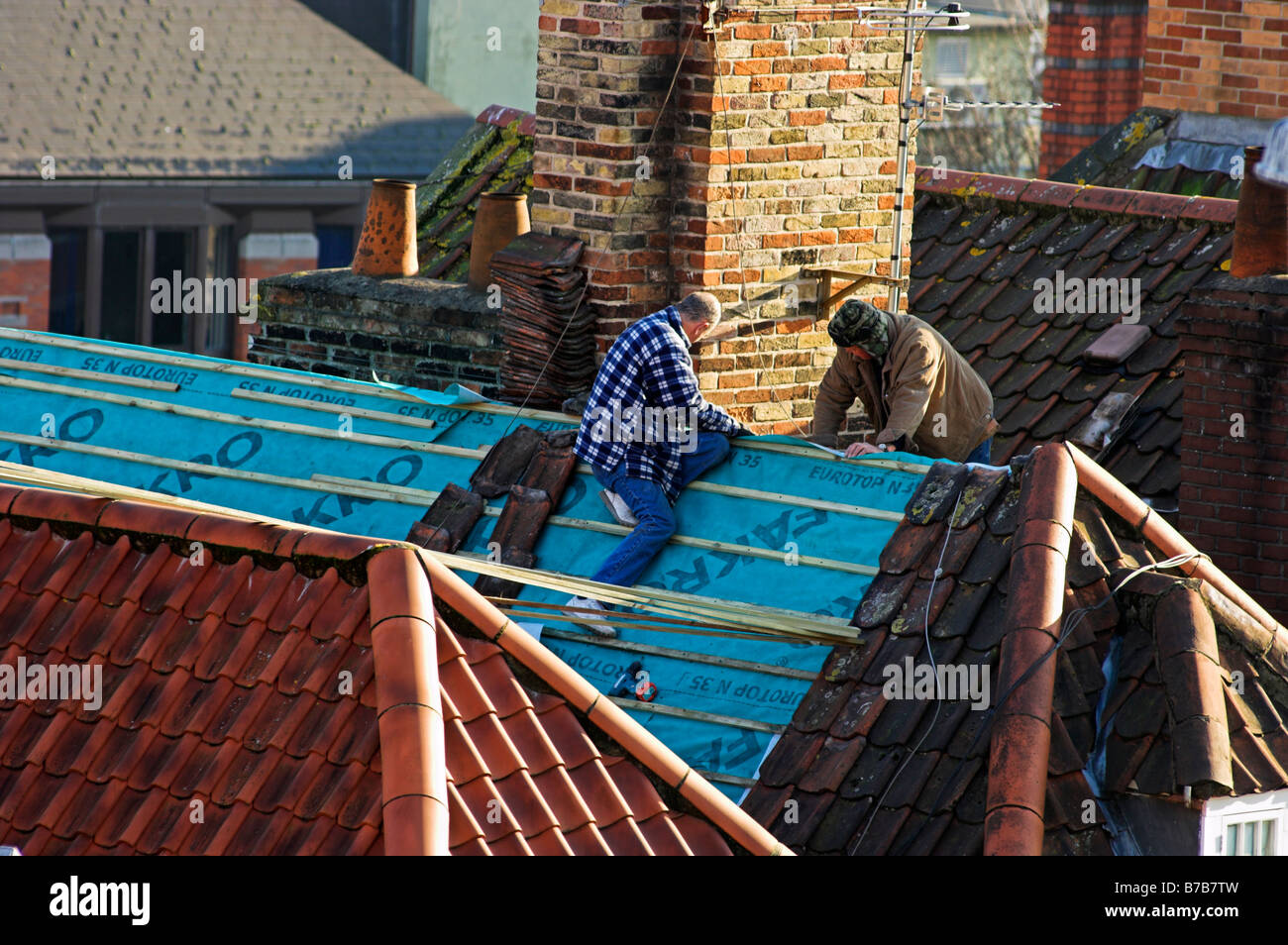 Workman sur le dessus de toit de tuiles faisant des réparations d'hiver Banque D'Images