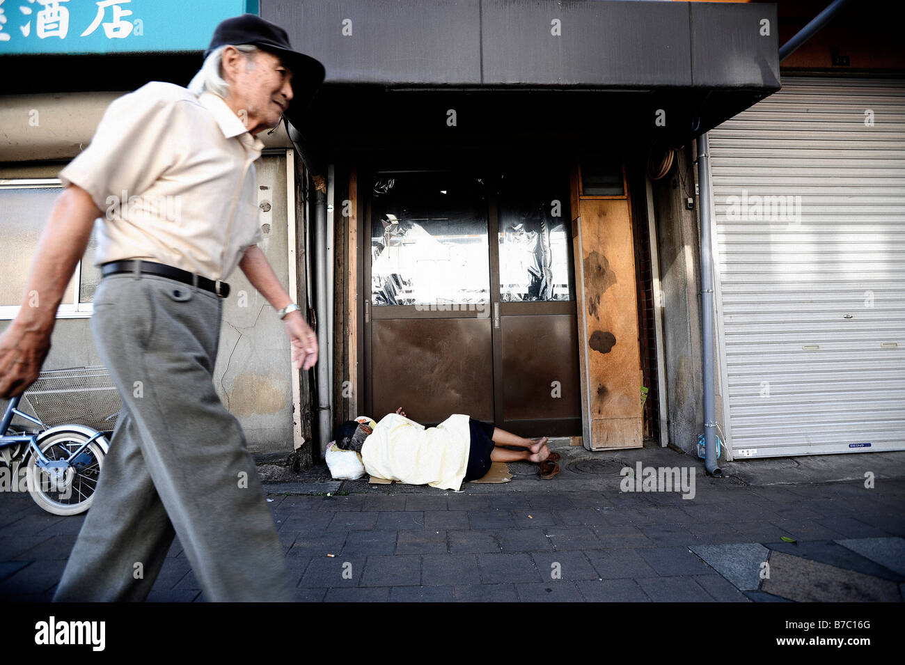 Un homme âgé marche dernières journalier d'un sans-abri dormant dans la porte d'un atelier fermé, à Osaka au Japon. Banque D'Images