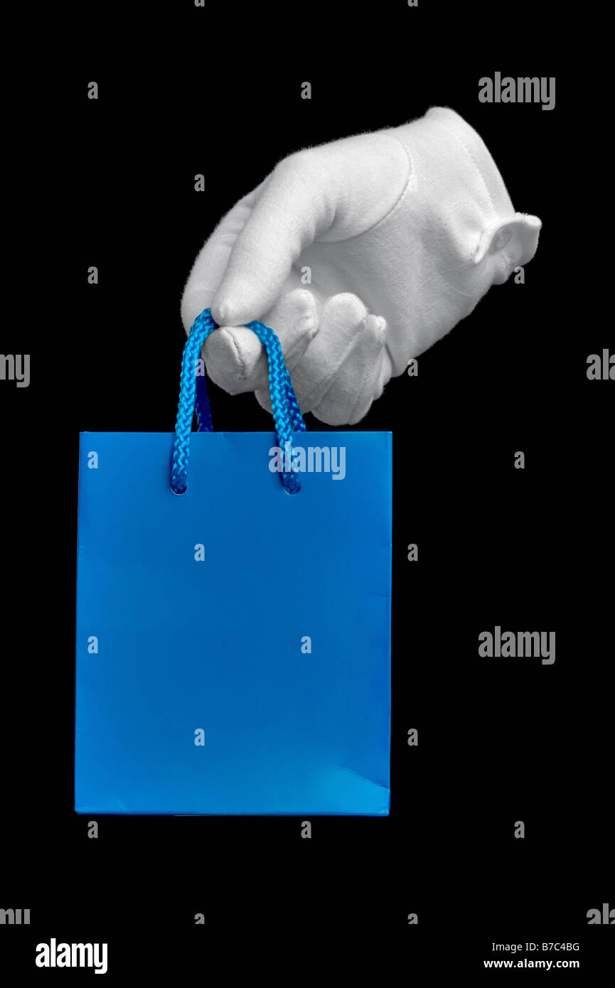 La main dans un gant blanc tenant un petit sac shopping bleu sur noir isolé Banque D'Images